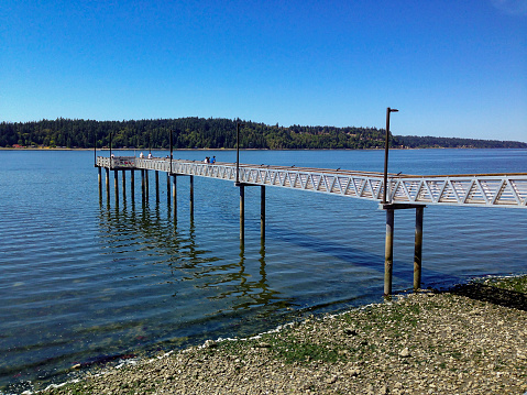 Port Orchard, Washington / USA - July 13, 2018: View of Port of Waterman Public Pier with people fishing in the clear water. Located in Port Orchard, a small city in Kitsap County, WA, near Bremerton and Seattle. Recreational pursuits include fishing, birding, scuba diving and sunbathing.