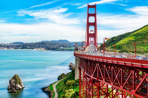 This image provides an alternate perspective of the iconic Golden Gate Bridge during rush hour traffic on a beautiful afternoon with the sky fill of clouds.