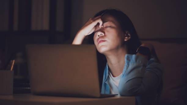 asiatische studentin oder geschäftsfrau arbeiten spät in der nacht. konzentriert und schläfrig am schreibtisch im dunklen raum mit laptop oder notebook. konzept von menschen hartarbeit und burnout-syndrom. - überstunde stock-fotos und bilder