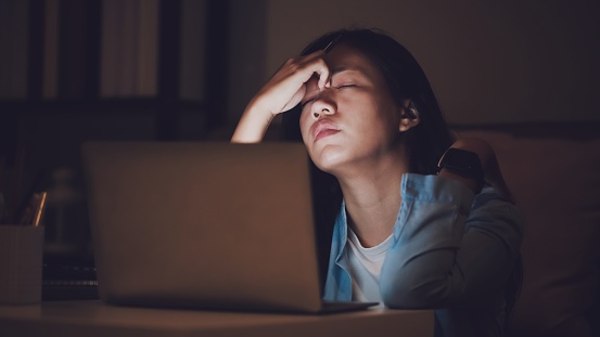 Una estudiante asiática o una empresaria trabajan hasta tarde por la noche. Concentrado y se sienta somnoliento en el escritorio en la habitación oscura con ordenador portátil o portátil. Concepto de personas de trabajo duro y síndrome de agotamiento. photo