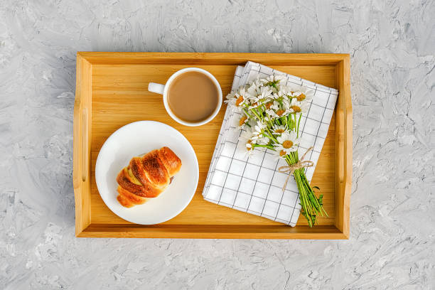 Cup of coffee with milk, freshly baked croissant, checkered napkin and camomile flowers on wooden tray on gray stone table. Concept Good morning Top view stock photo