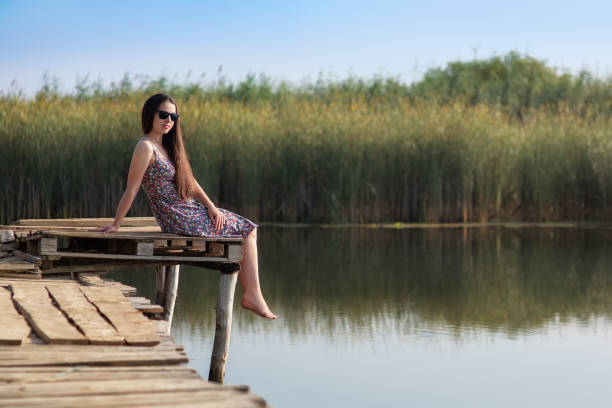 young woman sitting on wooden jetty on the river and dreaming