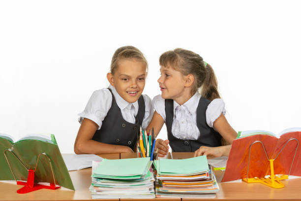 istock Two girls whisper while sitting at a desk 1167332440