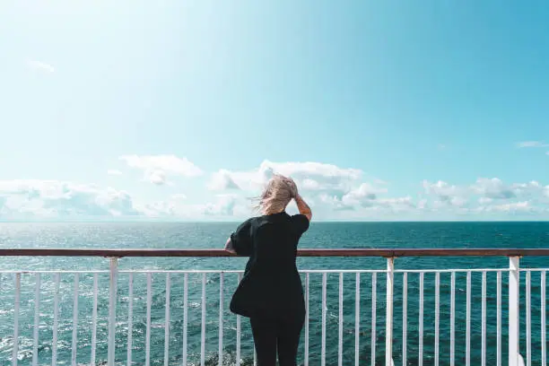 A young woman with tattoos is traveling on a ferry cruise in the Baltic Sea on a sunny summer day.