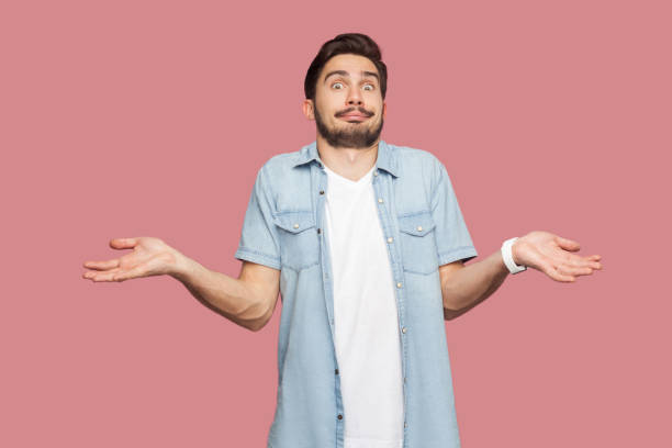 I don't know. Portrait of confused handsome bearded young man in blue casual style shirt standing with raised arms and looking at camera with answer. I don't know. Portrait of confused handsome bearded young man in blue casual style shirt standing with raised arms and looking at camera with answer. indoor studio shot, isolated on pink background. Confusion stock pictures, royalty-free photos & images