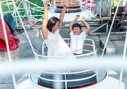 Beautiful Woman of Asian Ethnicity is Having a Lot of Fun Riding on Ferris Wheel with her Cute Little Son. Happy Mother and Son are Enjoying in Amusement Park on a Rollercoaster on a Warm Sunny Day.
