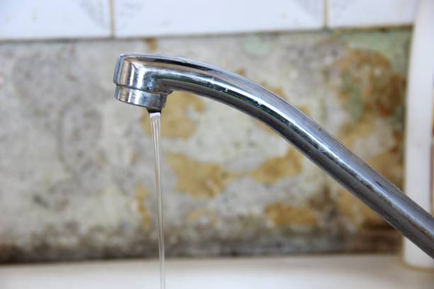 istock a thin stream of water flows from the tap, silver colored kitchen faucet on old wall background 1167348387