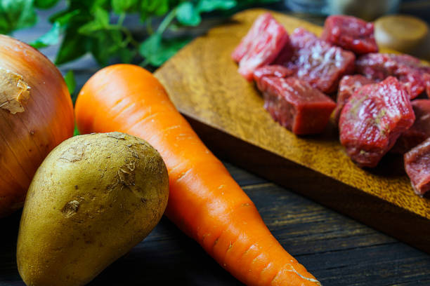 Raw unpeeled potatoes, onions, carrots, and beef on the wooden table