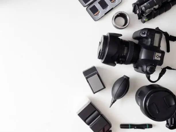 Photo of top view of work space photographer with digital camera, flash, cleaning kit, memory card, tripod and camera accessory on white table background