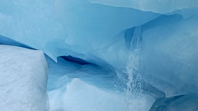Interior of an ice cave that is a white and blue glacier. Water flowing fast from melting ice. Steadicam, 4K