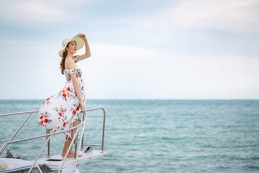 Summer vacation concept, Travel asian woman with dress and hat relax on sailboat in tropical sea at Pattaya, Thailand