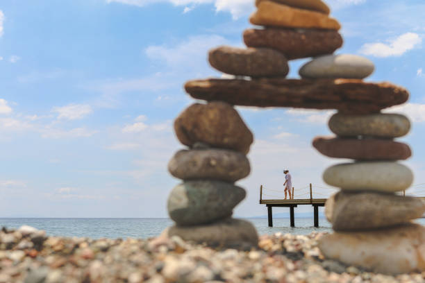 Young Woman walking on pier shown through a pebble tower on the beach at Assos, Canakkale of Aegean Sea in Turkey. (Selective Focus)