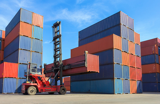 Forklift handling container box loading to truck in shipping yard with cargo container background.