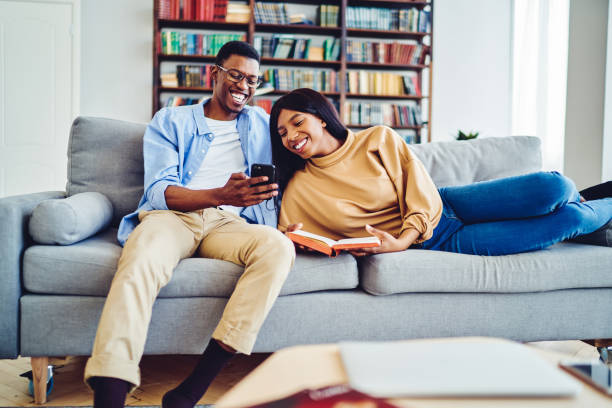 istock Smiling dark skinned couple in love having fun together resting at comfortable sofa in bright living room,happy african american guy showing video to girlfriend on mobile phone laughing at home 1167376886