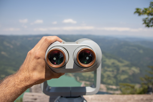 Male Hands Holding Observation Binoculars at Viewpoint. Panorama view from up high