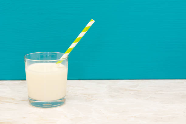 Creamy, fresh milk with a retro paper straw in a glass tumbler with a teal background and copy space