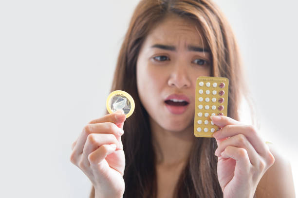молодая женщина, держащая презервативы и противозачаточные таблетки, предотвращает беременность - sexual issues aids condom human pregnancy стоковые фото и изображения