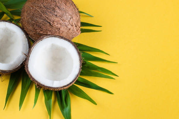 istock Ripe half cut coconut with green leaves on a yellow background. 1167378310