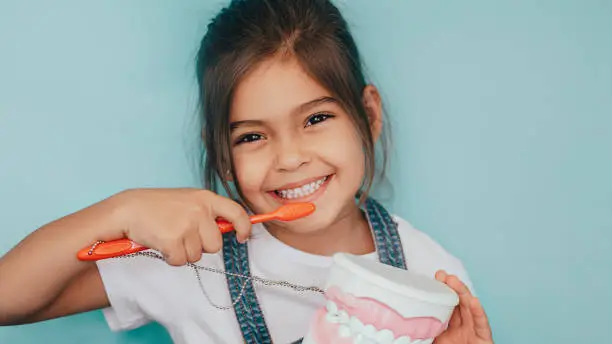 Photo of smiling mixed raced girl brushing teeth at blue background.