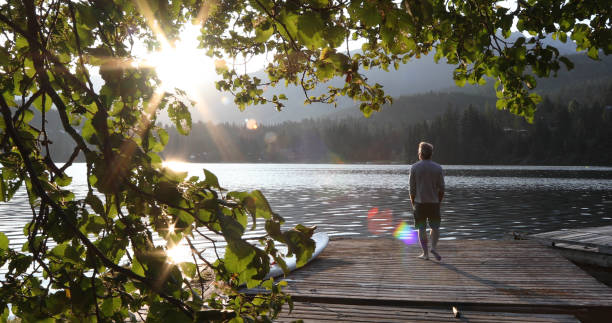 l'uomo cammina sul molo sul lago e guarda l'alba sulle montagne e sulla foresta - mind trip foto e immagini stock