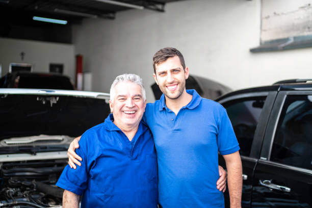 portrait of two mechanics standing in a repair shop (family business) - auto repair shop adult auto mechanic blue imagens e fotografias de stock