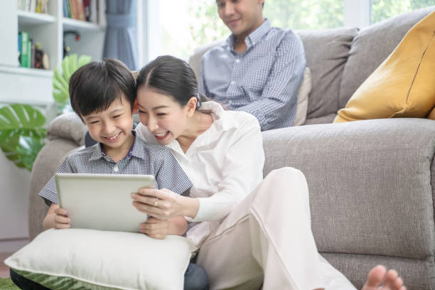 happy asian family spending time together on sofa in living room. family and home concept - couple laptop computer digital tablet imagens e fotografias de stock