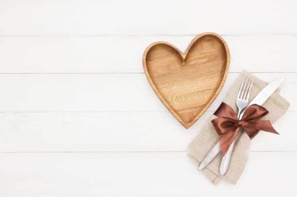 istock Place Setting. Empty wooden  plate, fork and knife on white  background.Wooden plate heart shape.Love food, love eating, romantic dinner , Valentine's day 1167402145