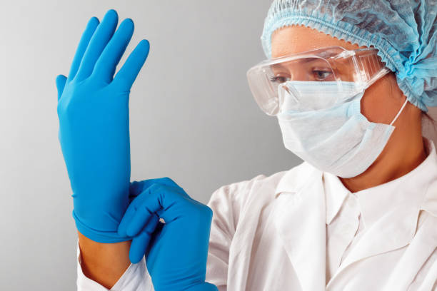 w laboratorium chemik naukowiec zakłada rękawice ochronne. mikrobiolog w sterylnej odzieży i goglach. - doctor preparation surgery surgical glove zdjęcia i obrazy z banku zdjęć