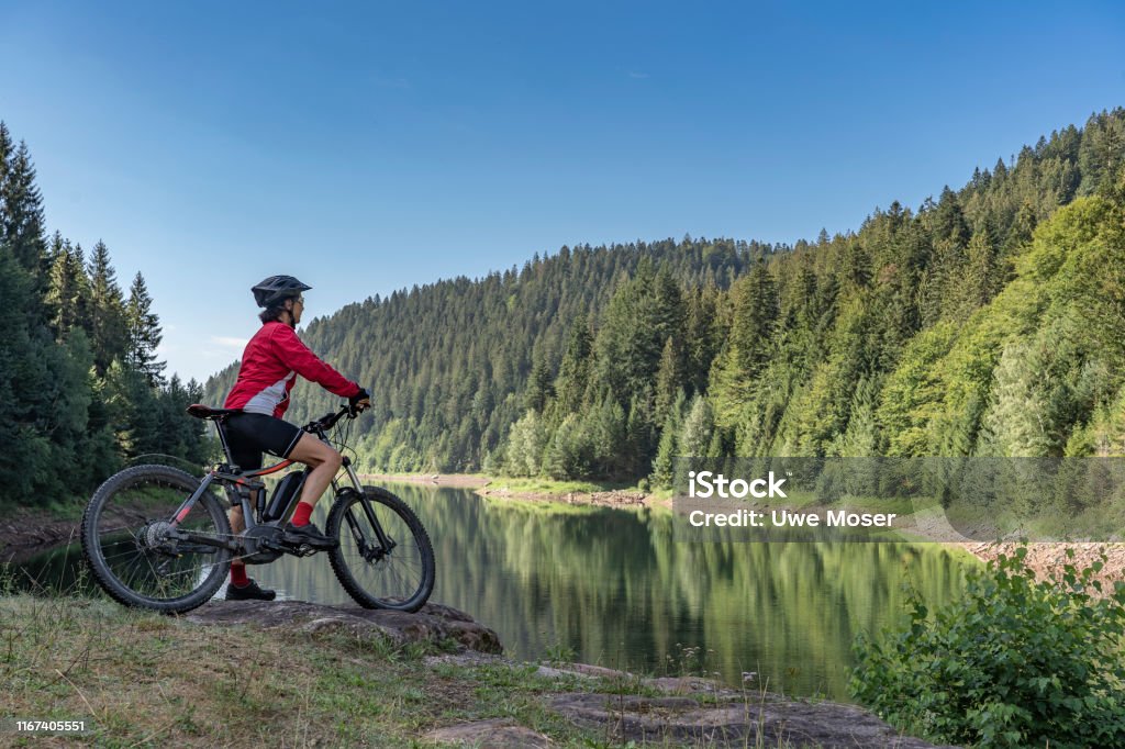 mountain biking in the black forest nice and ever young senior woman with her electric mountain bike at the Kinzig drinking Water reservoir in the northern Black Forest, Baden-Wuerttemberg, Germany Electric Bicycle Stock Photo
