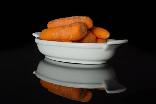 Photo of Orange baby carrot isolated on black glass