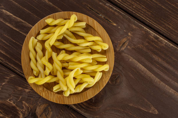 Raw pasta gemelli on brown wood Lot of whole raw pasta gemelli on bamboo plate flatlay on brown wood bamboo twist stock pictures, royalty-free photos & images