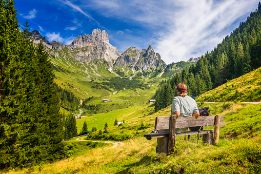 Young man sitting on bench and enjoys view on big Bischofsmütze, Dachstein mountains, alps