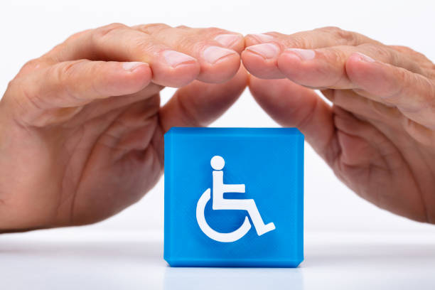 Close-up Of A Man's Hand Protecting Blue Cubic Block With Disabled Handicap Icon