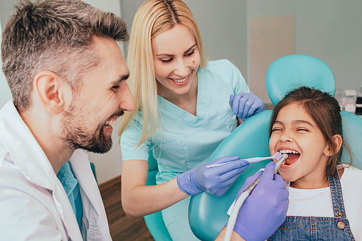 dentista y su asistente están tratando los dientes de una niña. Odontopediatría photo