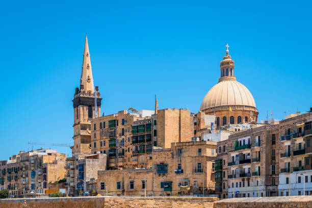 View of cathedral and belltower in old city centre of Valletta, Malta. Typical architecture in the city center of Valletta with church and cathedral as highlights. Sand-colored brick high buildings with colored balconies and clear blue sky on a beautiful summer day. st paul cathedral la valletta malta island stock pictures, royalty-free photos & images