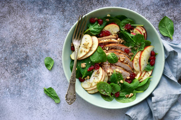 Spinach salad with grilled chicken breast, red apple, dried cranberry and walnuts Spinach salad with grilled chicken breast, red apple, dried cranberry and walnuts in a bowl on a light grey slate, stone or concrete background. Top view with copy space. green apple slice overhead stock pictures, royalty-free photos & images