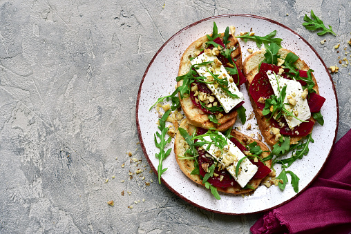 Healthy toasts with beetroot, feta cheese, nuts and arugula on a plate over grey slate, stone or concrete background.Top view with copy space.
