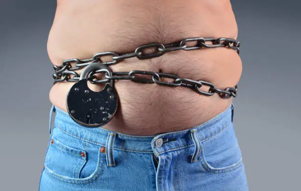 Photo of Diet concept. Big belly coiled with chain and lock.
