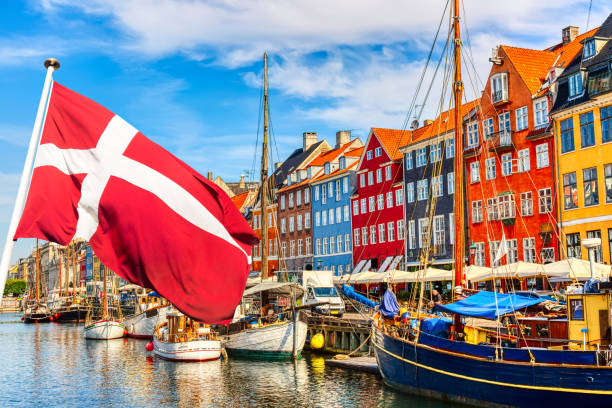 vista iconica di copenaghen. famoso vecchio porto di nyhavn nel centro di copenaghen, in danimarca, durante la giornata di sole estivo con la bandiera della danimarca in primo piano. - copenhagen foto e immagini stock