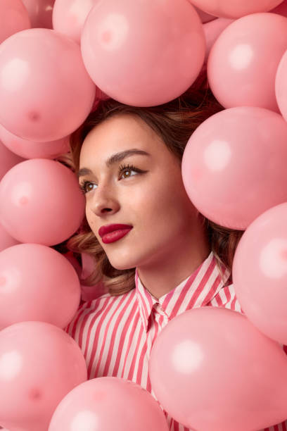 Dreamy female amidst balloons Sensual young woman with bright makeup looking away thoughtfully among pink balloons vogue cover stock pictures, royalty-free photos & images