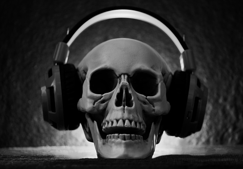 Skull music with headphone / Human skull listening to music earphone decorated at halloween party and light on dark background