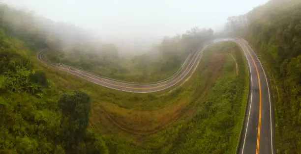 Photo of Panorama of aerial view over mountain road going through forest with rain fog
