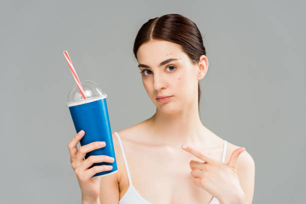 istock woman with acne on face pointing with finger at plastic cup with straw isolated on grey 1167481205