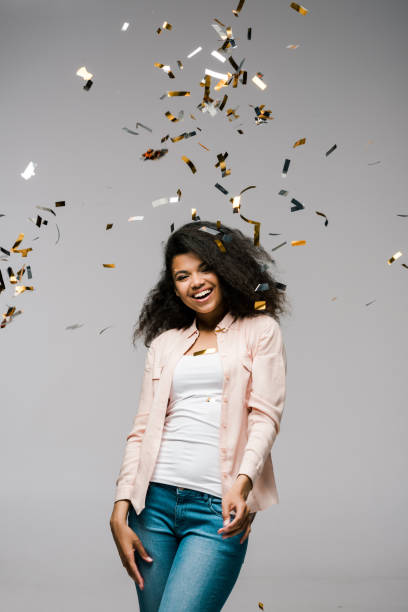 istock young african american woman smiling near falling confetti while standing on grey 1167483138