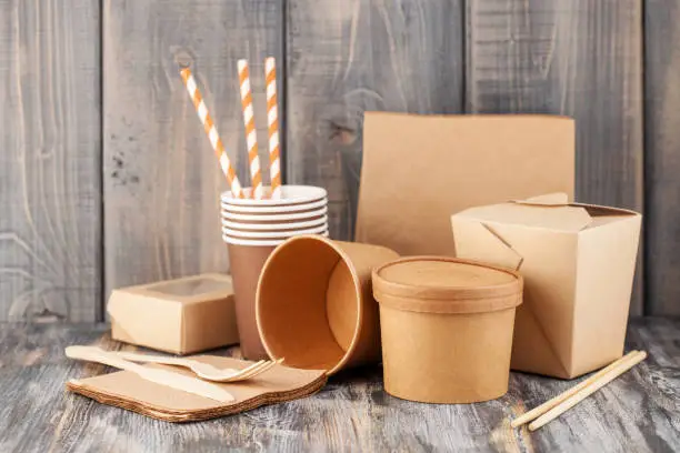 Eco craft paper tableware. Paper cups, dishes, bag, fast food containers and  wooden cutlery on wooden background. Recycling concept. Copy space