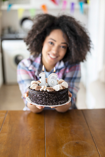 Smiling woman holding birthday cake with candles, looking at camera.