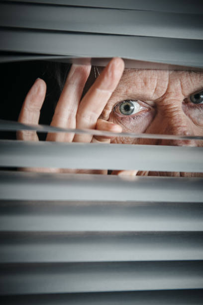 istock Panic-stricken senior woman peering through blinds 1167498166