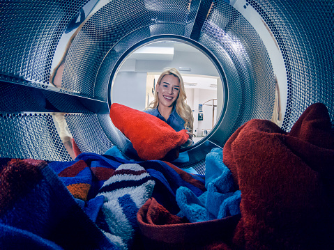 Young woman doing laundry hes weekly washing in a self-service public laundry. View from the washing machine