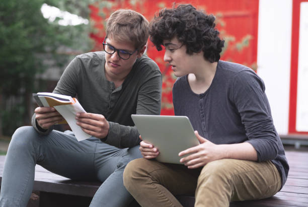 Two teenagers doing homework with books and a cosplay, sitting on the street on campus stock photo