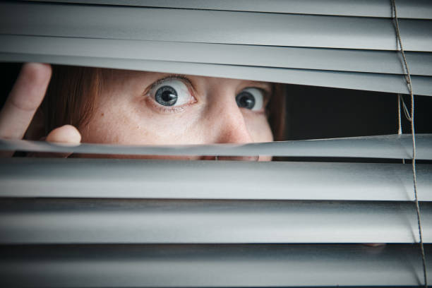 istock Scared young woman peeks through venetian blind 1167498845